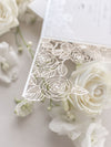 Intricato dettaglio di rose tagliate al laser con invito al giorno delle nozze avvolgente in lamina di perle