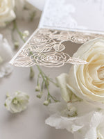 Intricato dettaglio di rose tagliate al laser con invito al giorno delle nozze avvolgente in lamina di perle